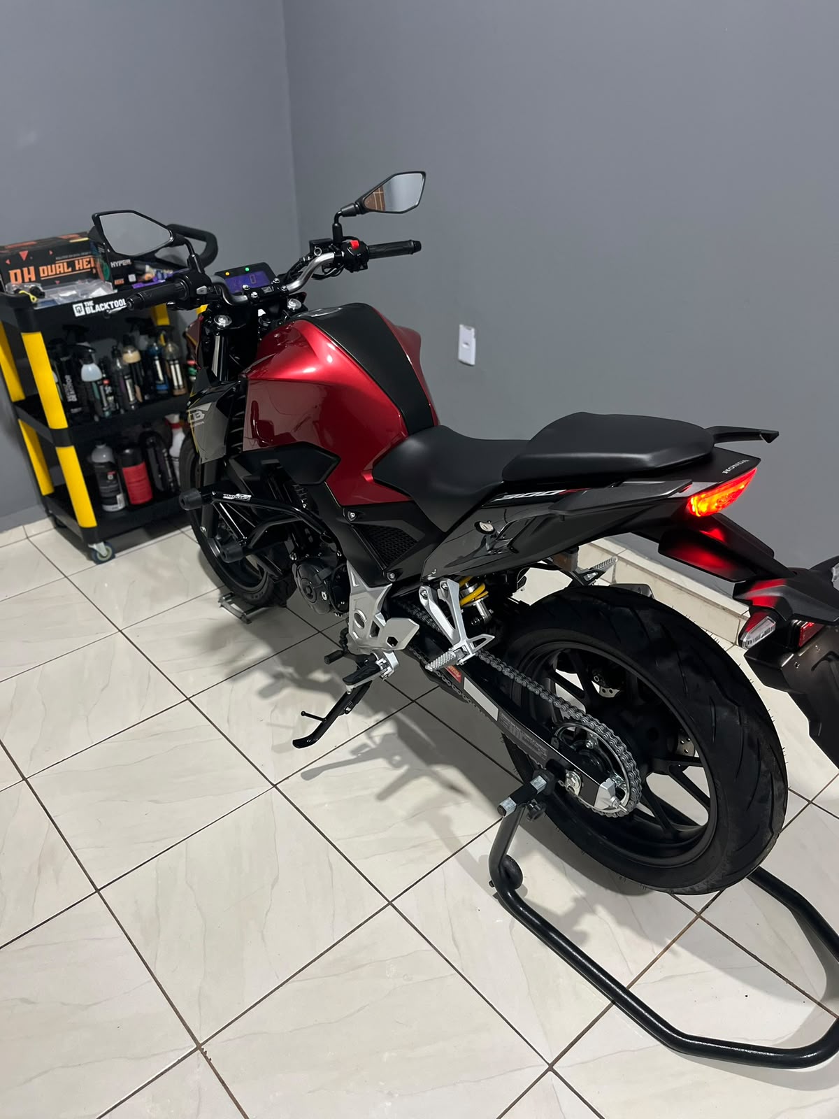 Honda CB vermelha na Zelon, com a luz refletindo na pintura do tanque